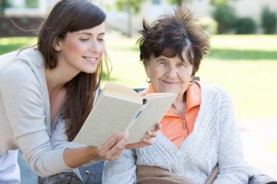 Symbolbild für Bildung und Soziales; Junge Frau liest Seniorin aus einem Buch vor